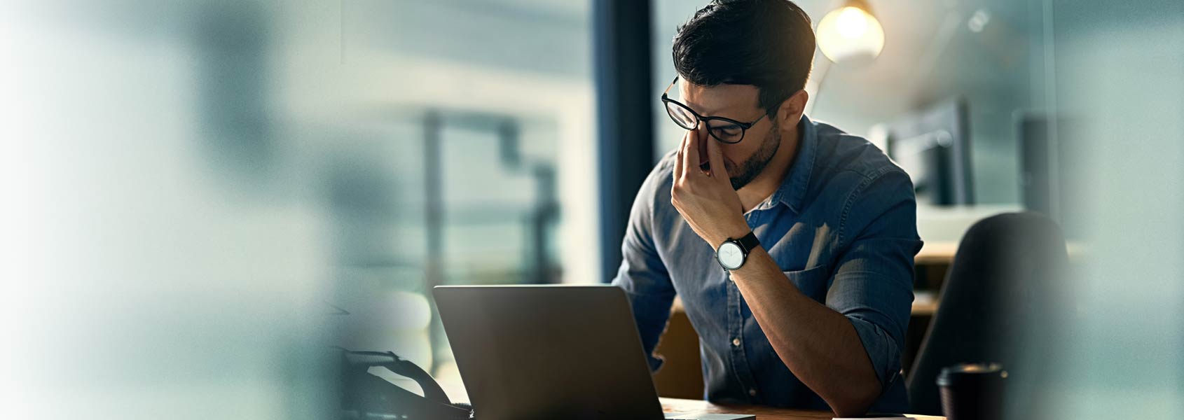 man pushing up glasses to rub eyes in front of laptop