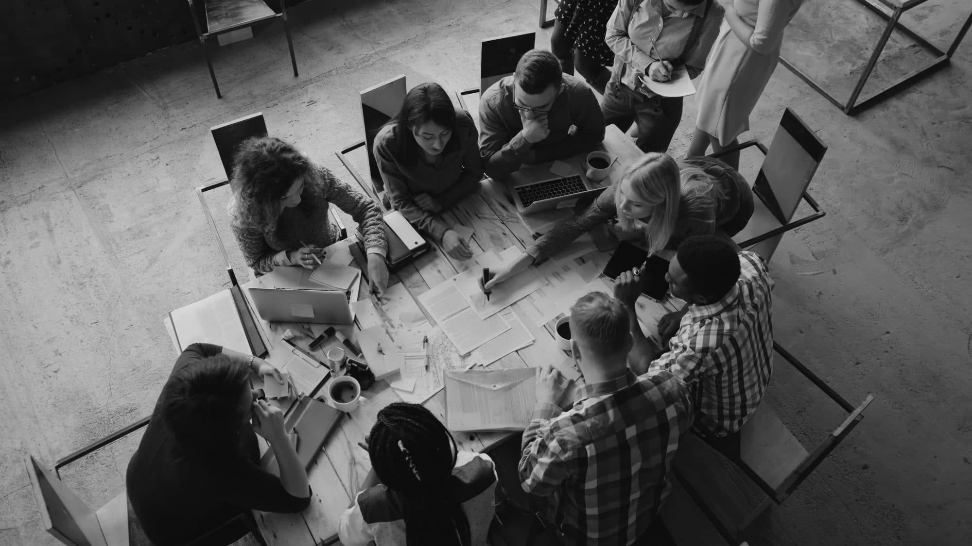 Top view of mixed race business team sitting at the table at loft office and working. Woman manager brings the document
