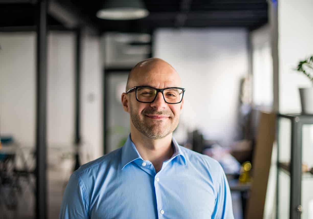 a man in a blue business shirt wearing glasses and smiling