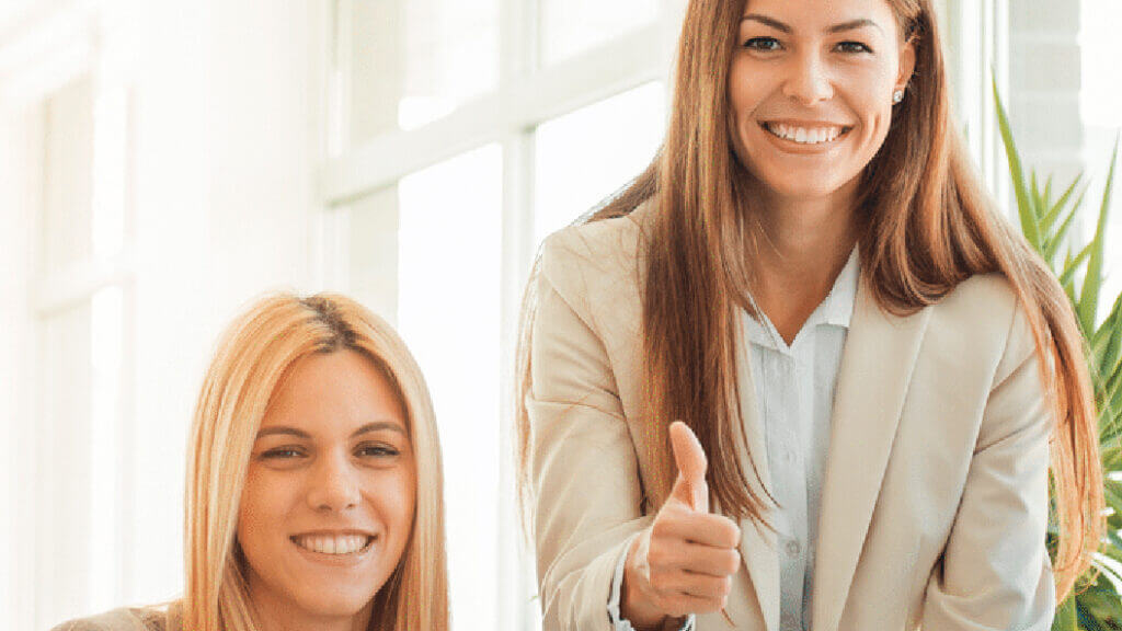 Two women smiling, one with their thumb up