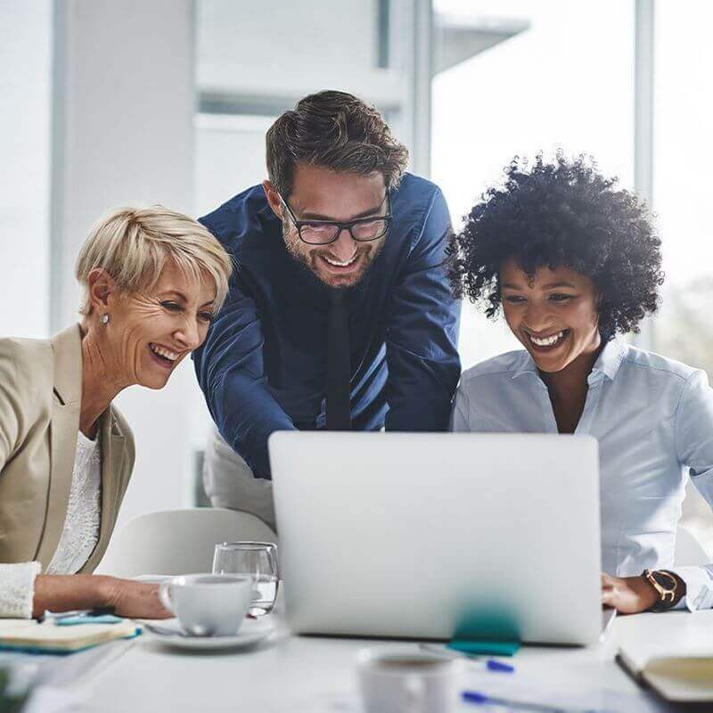 Three people gathered around a laptop and smiling