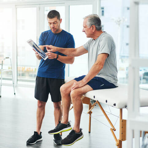 A man in physical therapy point at a tablet another man is holding