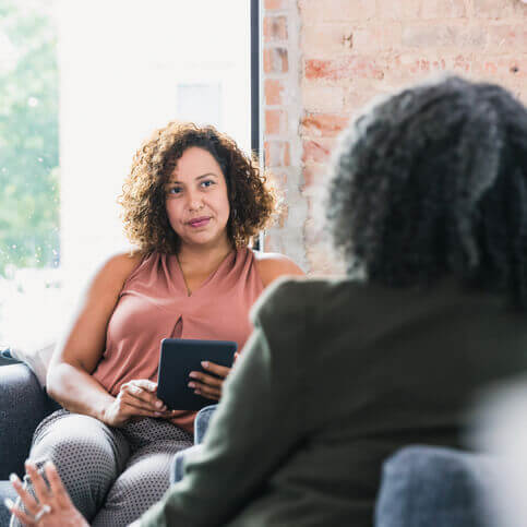 Two women speaking, with one holding a tablet