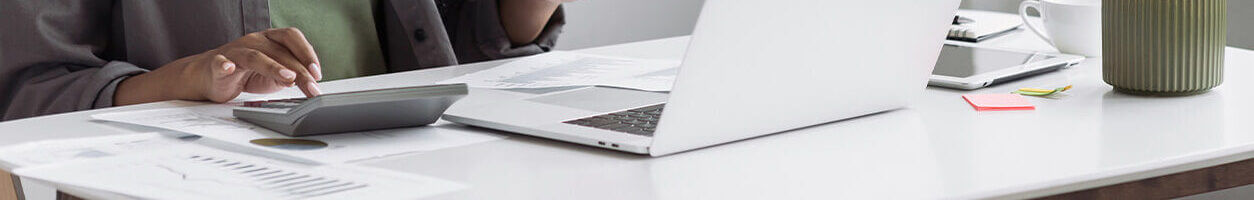 A women using a calculator surrounded by papers and a laptop