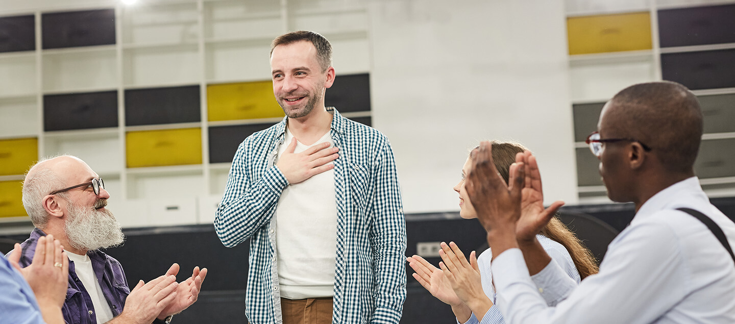 A man standing and speaking to a group of people who are applauding