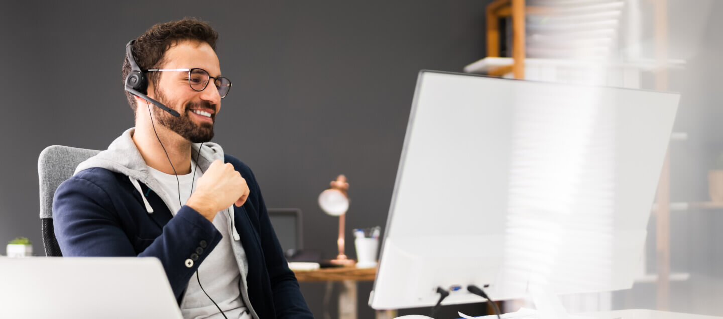 A man in a headset smiling at a computer